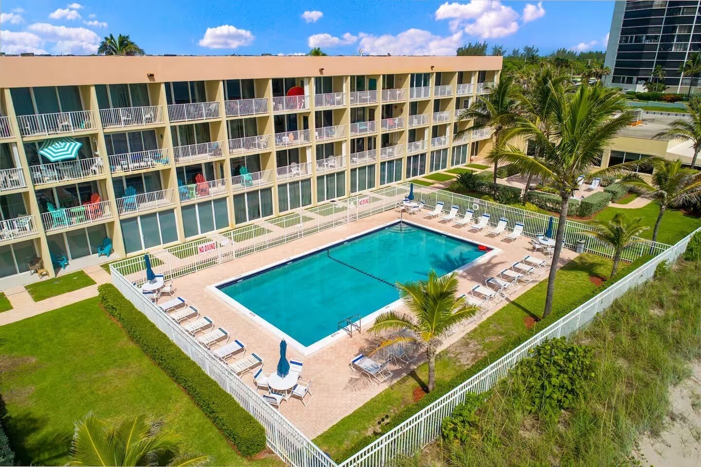 Un hotel con piscina rodeada de tumbonas y palmeras.