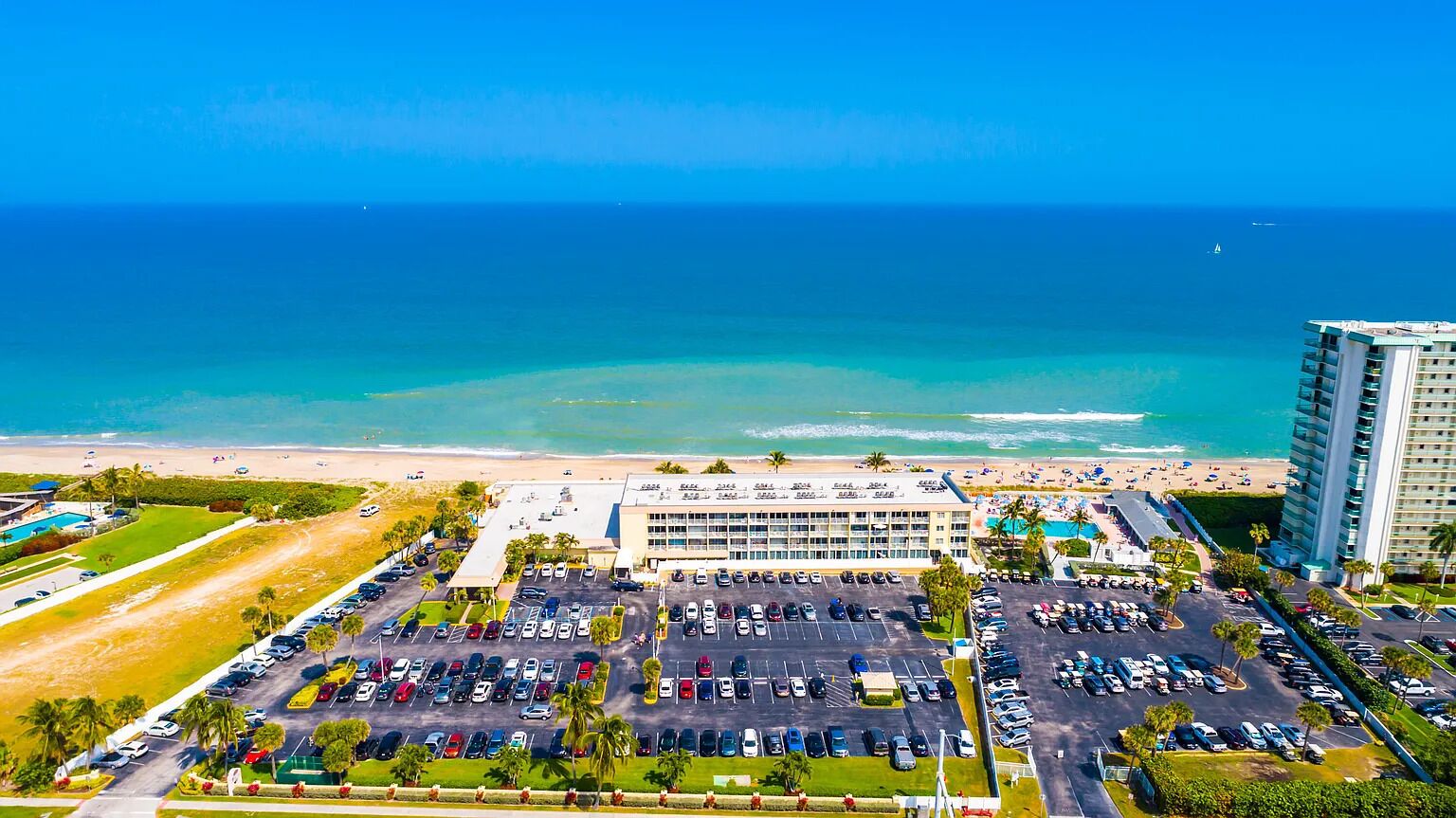 An aerial view of a hotel with a parking lot, beach, and ocean.
