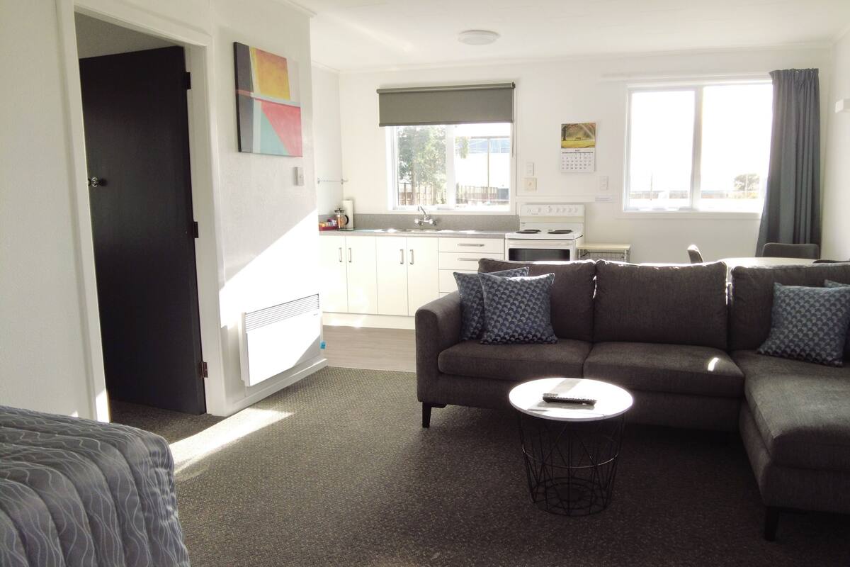A living room with a sofa, a coffee table, and a kitchen in the background.