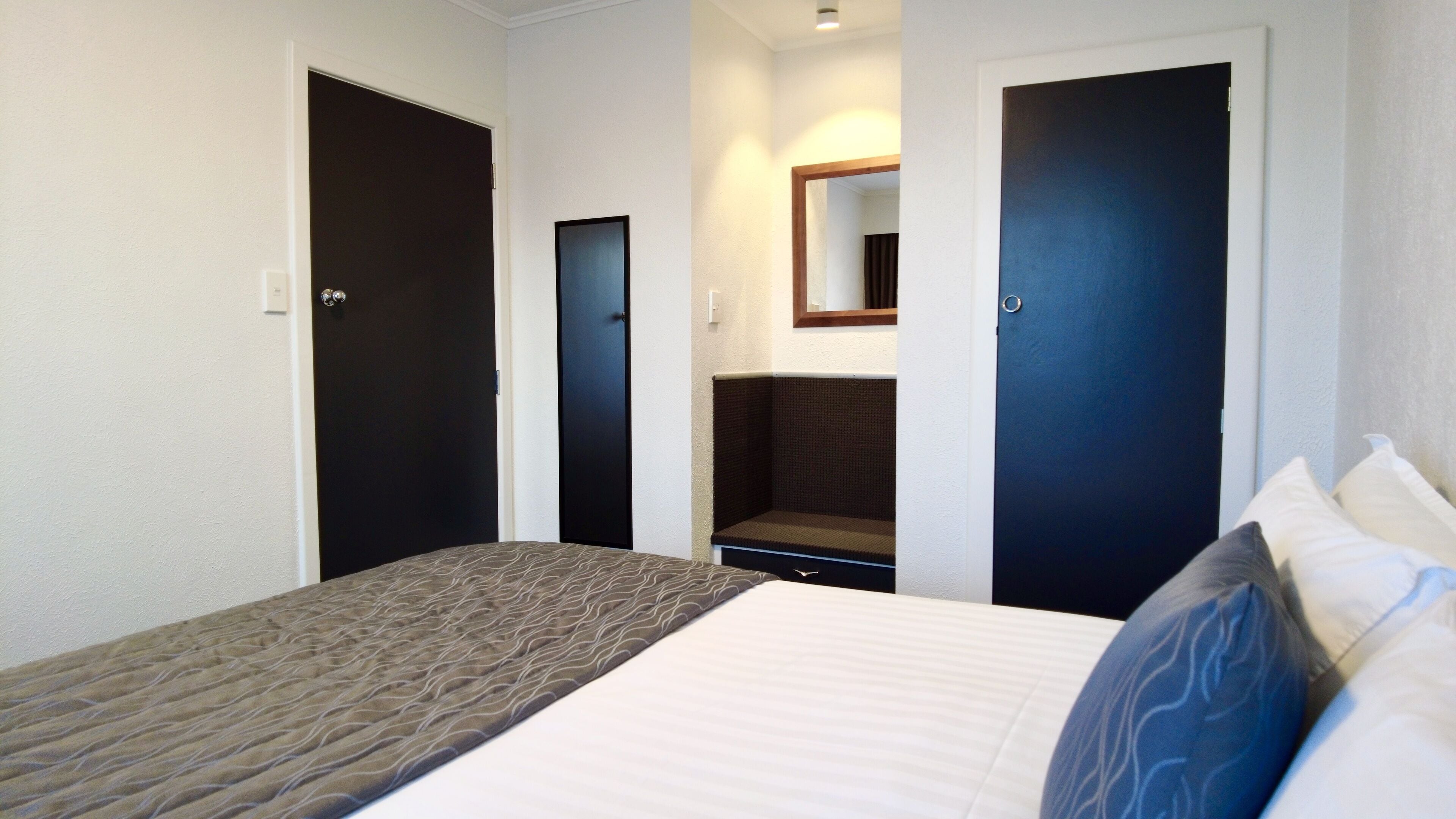 A hotel room with a bed, two doors, a mirror, and a chair.