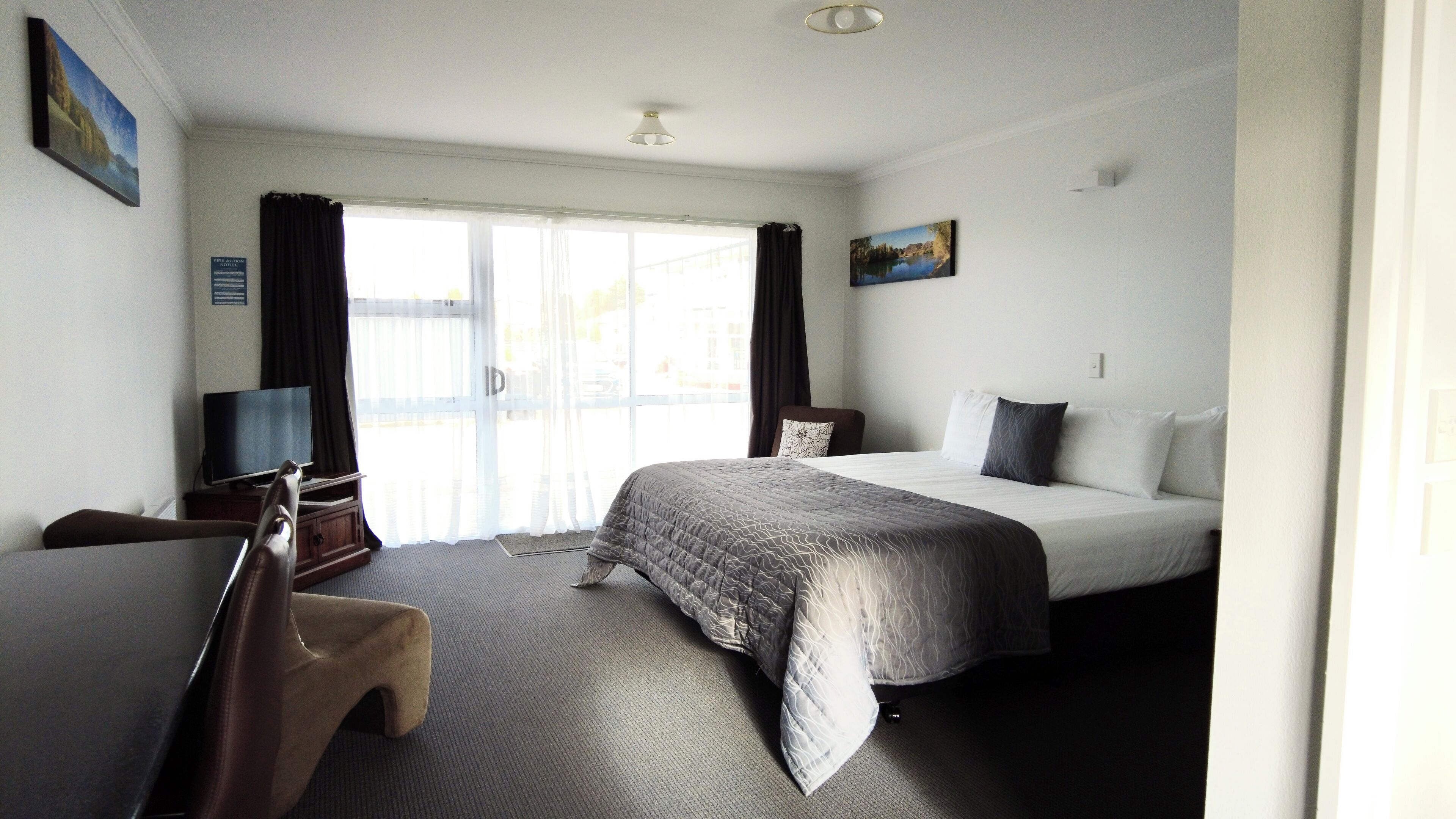 A hotel room with a bed, a desk, a chair, a TV, and a painting on the wall.