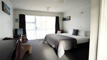 A hotel room with a bed, a desk, a chair, a TV, and a painting on the wall.
