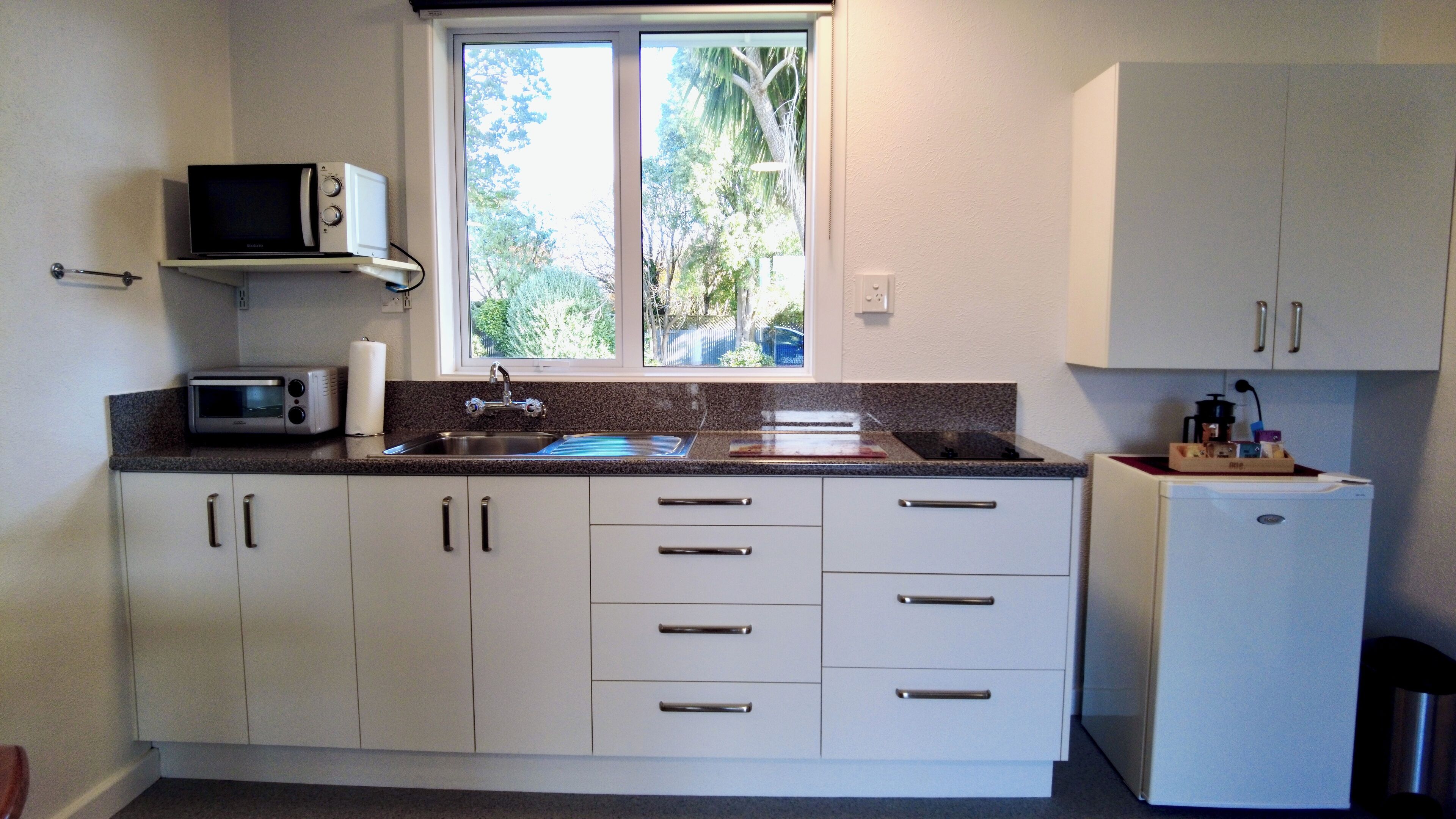 A compact kitchen with white cabinets, a microwave, a sink, and a refrigerator.