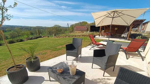 Eine Terrasse im Freien mit Korbmöbeln, einem Tisch mit einem Getränk und Blick auf die Landschaft.