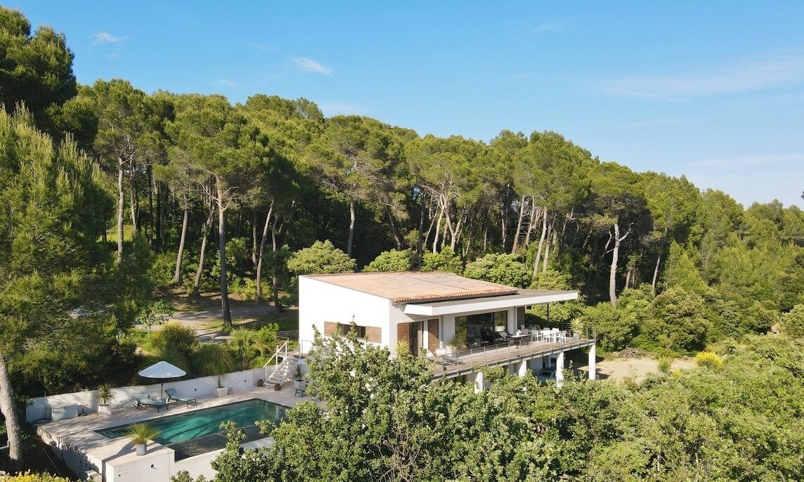 A modern house with a swimming pool, surrounded by dense forest.