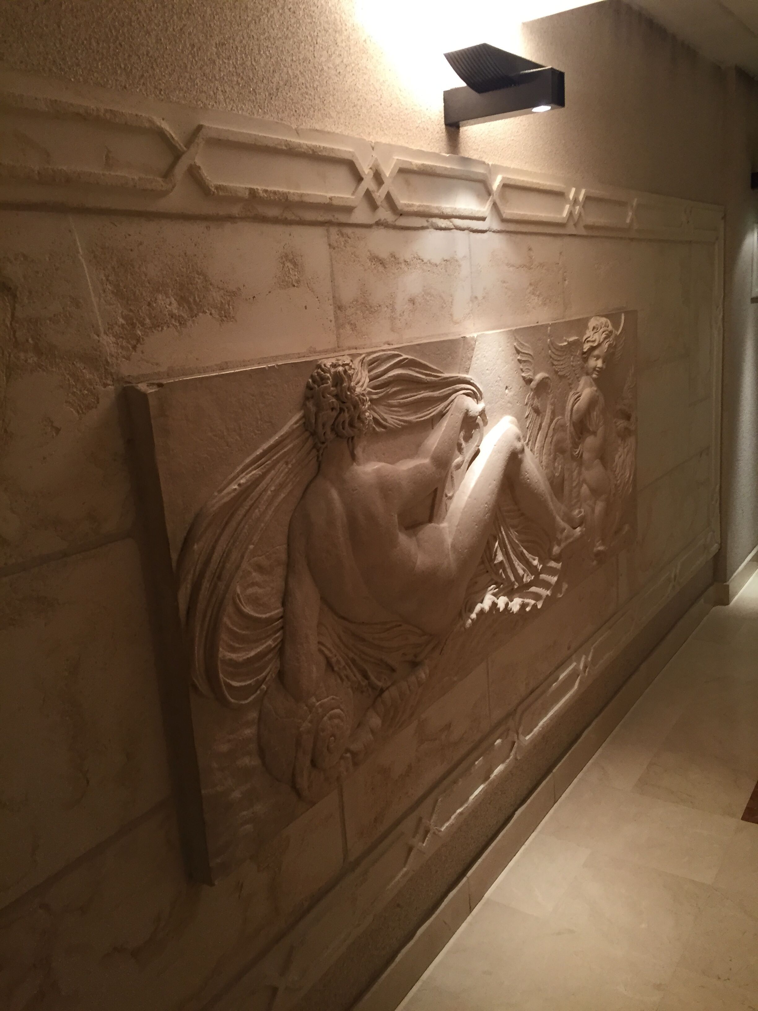 Un muro di marmo con un rilievo raffigurante una figura sdraiata e un angelo.