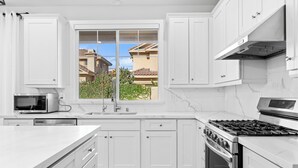 A modern kitchen with white cabinets, a built-in microwave, a stainless steel stove, and a large window offering a view of neighboring houses. - 4 New Construction in 2024 luxury home 4B/4.5B (Temple City)