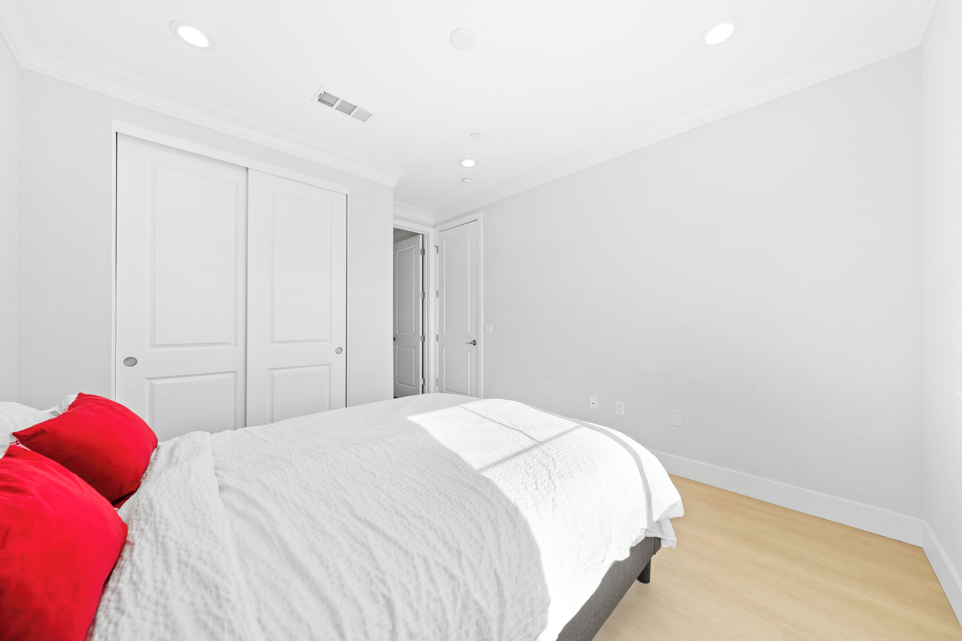 A bedroom with a bed, white walls, and a wooden floor.