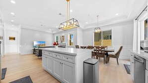A modern kitchen with white cabinets, a central island, and a dining area with wooden chairs. - 4 New Construction in 2024 luxury home 4B/4.5B (Temple City)