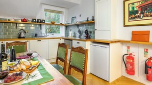 Cocina compacta con comedor, mostrando una mesa de madera dispuesta para una comida, un refrigerador pequeño y una ventana que proporciona luz natural.