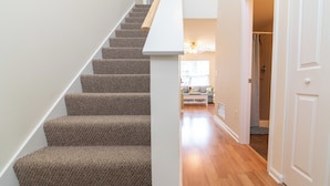 A staircase with carpeted steps leading to a second floor. A white wall and wooden floor are visible.