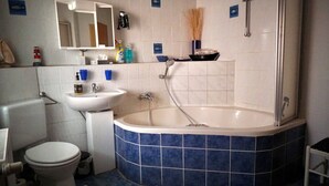 A bathroom with a white sink, a toilet, a bathtub with blue tiles, a shower, and a mirror above the sink. - Midgard vacation apartment in Sagenharz - Family apartment, 2 bedrooms & WLAN (Thale)