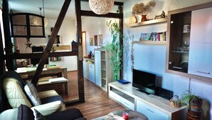 A cozy living room with a wooden staircase, a television, and a bookshelf. - Midgard vacation apartment in Sagenharz - Family apartment, 2 bedrooms & WLAN (Thale)