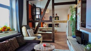 A living room with a sofa, a round coffee table, and a staircase leading to an upper level. - Midgard vacation apartment in Sagenharz - Family apartment, 2 bedrooms & WLAN (Thale)