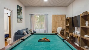 Une table de billard avec des billes, un canapé, une chaise, un téléviseur et un meuble en bois.
