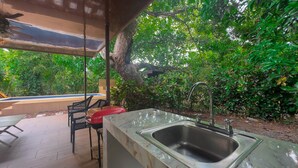 Une cuisine extérieure équipée d’un évier, de chaises, et avec une piscine en arrière-plan.