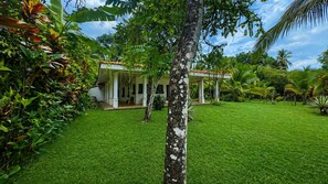 A house with a covered porch, surrounded by lush greenery and a well-maintained lawn. - Casa Ylang Ayala, pool home minutes to the sand! (Palo Seco Beach, Parrita,)