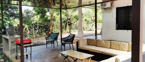 Un espace extérieur aménagé, abrité et doté d’un canapé, de deux fauteuils, d’une table et d’un barbecue.