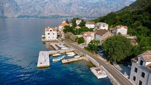 Un villaggio costiero con edifici in pietra, un porto turistico e montagne sullo sfondo.