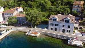 Un edificio costiero con facciata in pietra, tetto in tegole e un molo con una barca.