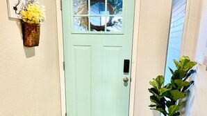A light green door with a window, a doormat, a potted plant, and a wall-mounted light switch. - Round Rock - Austin Hideaway (Round Rock)