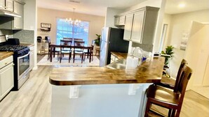 A modern kitchen with a central island, stainless steel appliances, and a dining area with a table and chairs. - Round Rock - Austin Hideaway (Round Rock)