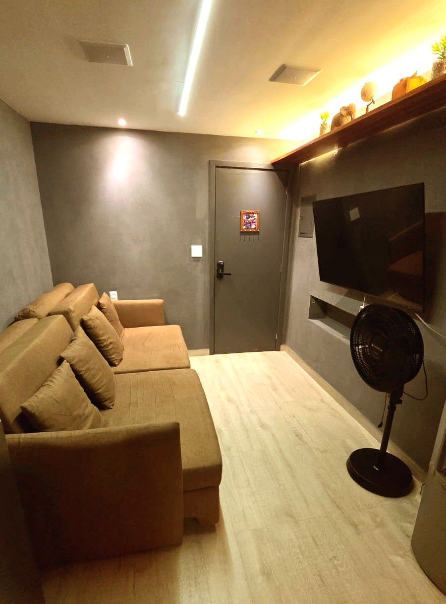 Uma sala de estar com sofá, televisão, ventoinha e porta.