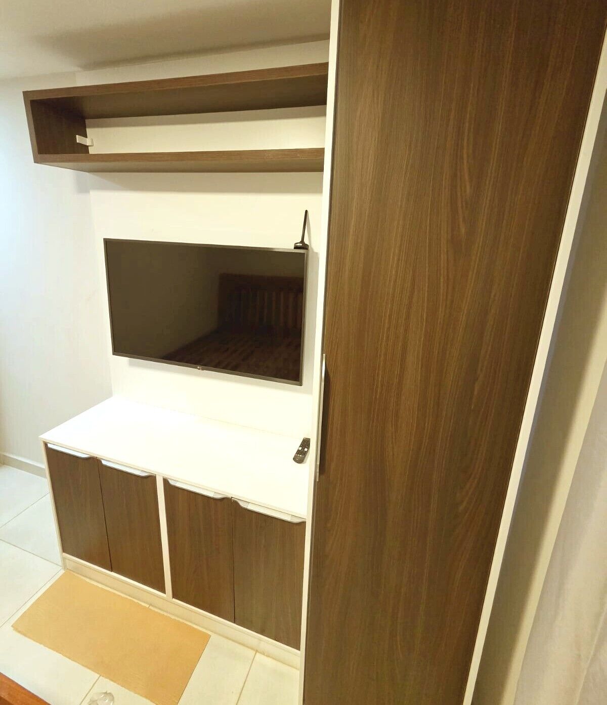 A room with a built-in TV shelf, a wardrobe, and a small seating area.