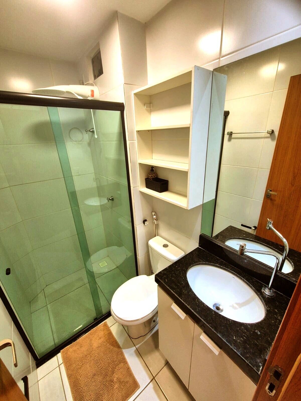 Un baño moderno con cabina de ducha de vidrio, inodoro blanco, lavabo con encimera negra y espejo sobre el lavabo.