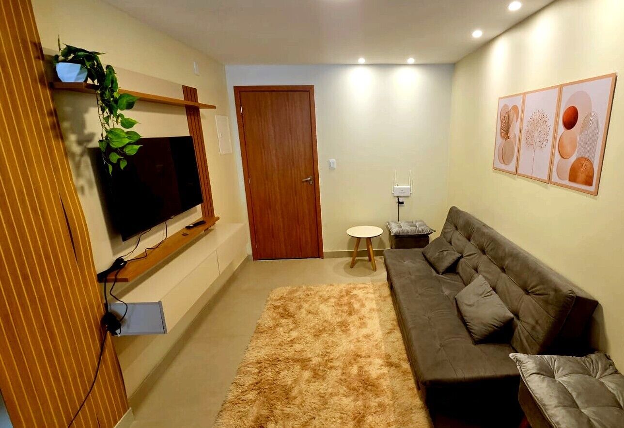 A living room with a sofa, a TV mounted on the wall, a small round table, and a door in the background.