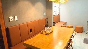 A dining area with a wooden table, cushioned bench seating, wicker pendant lights, and a wall-mounted shelf with decorative items.