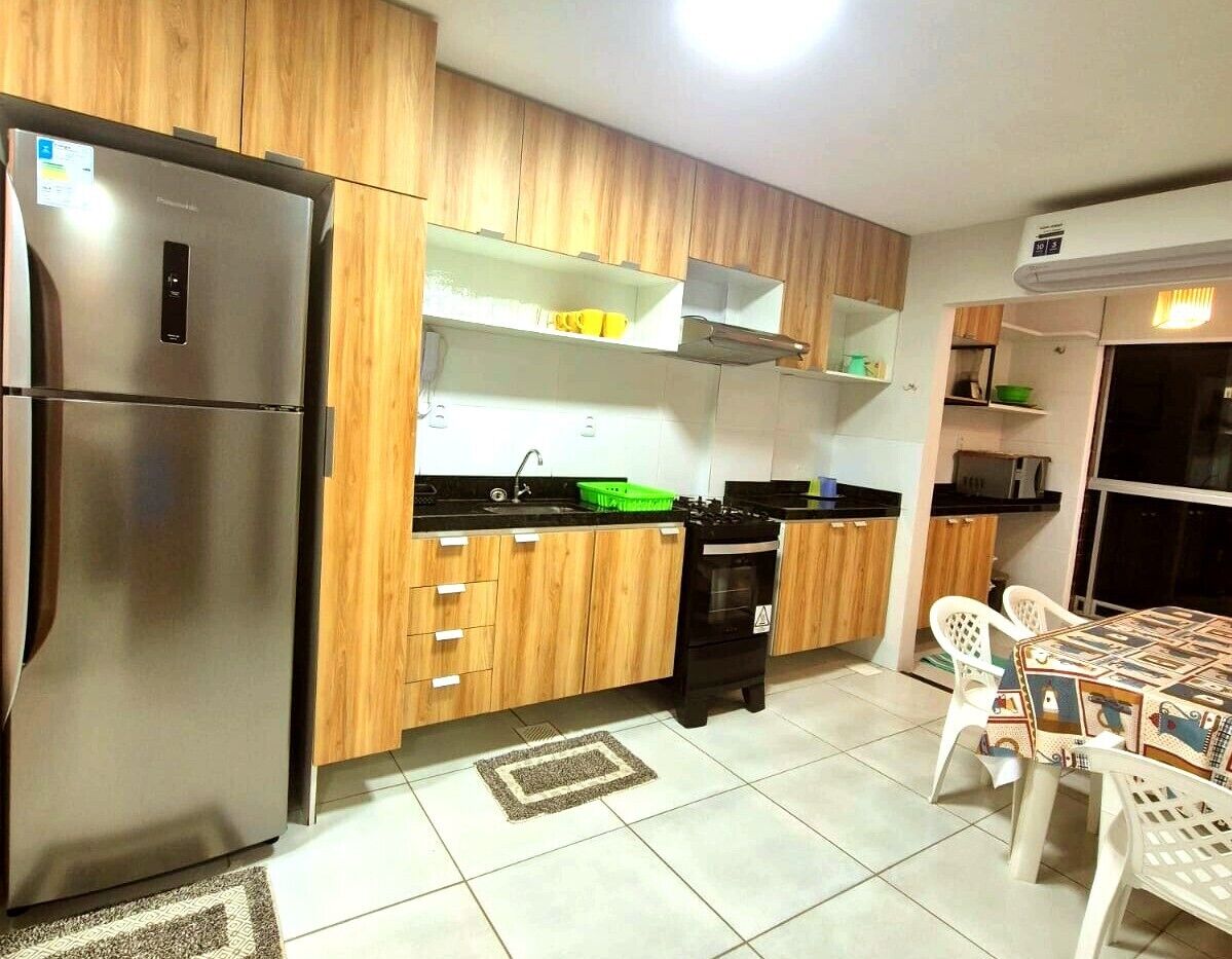 A modern kitchen with wooden cabinets, a stainless steel refrigerator, a black stove, and a dining table with chairs.