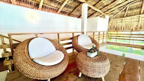 A thatched-roof room with two woven chairs and a small table, wooden flooring, and a view through a wooden railing. - Beachfront Luxury Villa in Amatecampo Beach, El Salvador (Amatecampo)