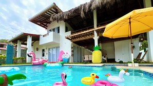 A swimming pool with various inflatable toys, a thatched roof structure, and a yellow umbrella. - Beachfront Luxury Villa in Amatecampo Beach, El Salvador (Amatecampo)