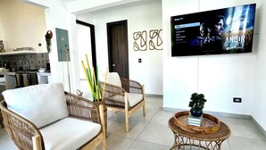 A modern living room with wicker furniture, a flat-screen TV, and a kitchen in the background. - Beachfront Luxury Villa in Amatecampo Beach, El Salvador (Amatecampo)