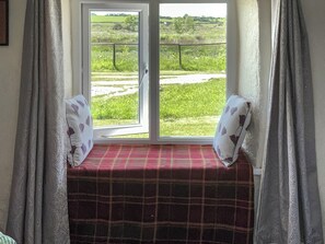 A window seat with a plaid cushion, curtains, and a view of a green landscape.