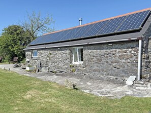 A stone building with a sloped roof, solar panels, a chimney, and a small window.