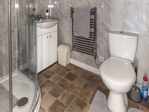 A bathroom with a glass-enclosed shower, a white sink with a soap dispenser, a toilet, and a towel rack.