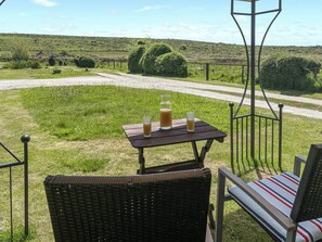 A wicker chair and a table with drinks, a metal fence, and a gravel path in a grassy field.