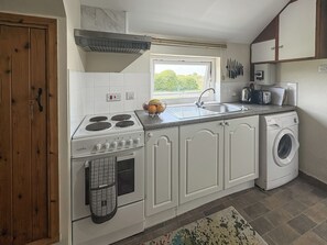 A kitchen with a stove, sink, and washing machine, wooden cabinets, and a window.