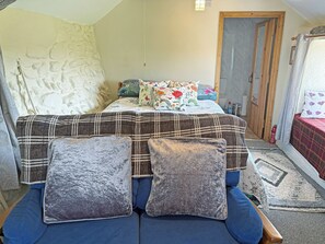 A bedroom with a bed, a sofa, a door, and a small table.