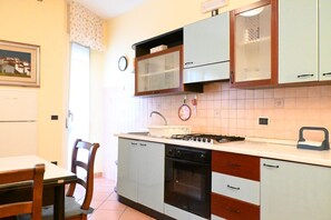 A compact kitchen with a stove, oven, and sink, a dining table with chairs, and a clock on the wall.