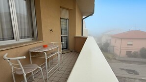 A balcony with a table and chairs, a window with blinds, and a view of a street and buildings. - SE152 - Senigallia, delightful two-room apartment facing the sea (Senigallia)