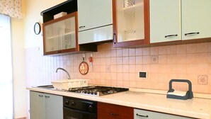 A kitchen with a gas stove, oven, and a sink. There are cabinets with handles and a clock on the wall. - SE152 - Senigallia, delightful two-room apartment facing the sea (Senigallia)