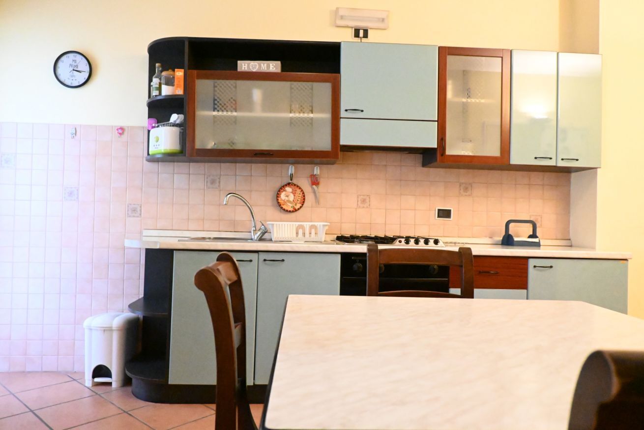 A kitchen with a sink, stove, cabinets, and a clock on the wall.