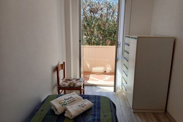 Una habitación pequeña con cama, una silla, un armario y vistas a un balcón con plantas.
