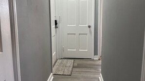 A hallway with a white door, a doormat, and a wooden floor. - Amazing Downtown Location! Quiet & Spacious! #C (Mount Vernon)