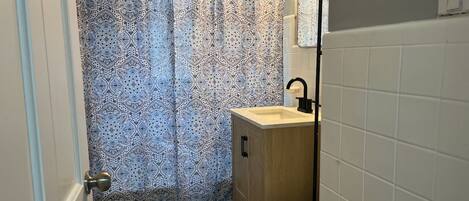 A bathroom with a patterned shower curtain, a wooden cabinet, a sink, and a toilet.