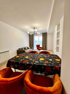Ein modernes Wohnzimmer mit Esstisch, orangefarbenen Sesseln, einer Couch und Blick auf die Stadt durch große Fenster.