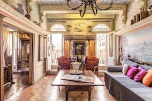 Classic design meets comfort in this elegant room, featuring a grand chandelier, ornate moldings, and a large painting.